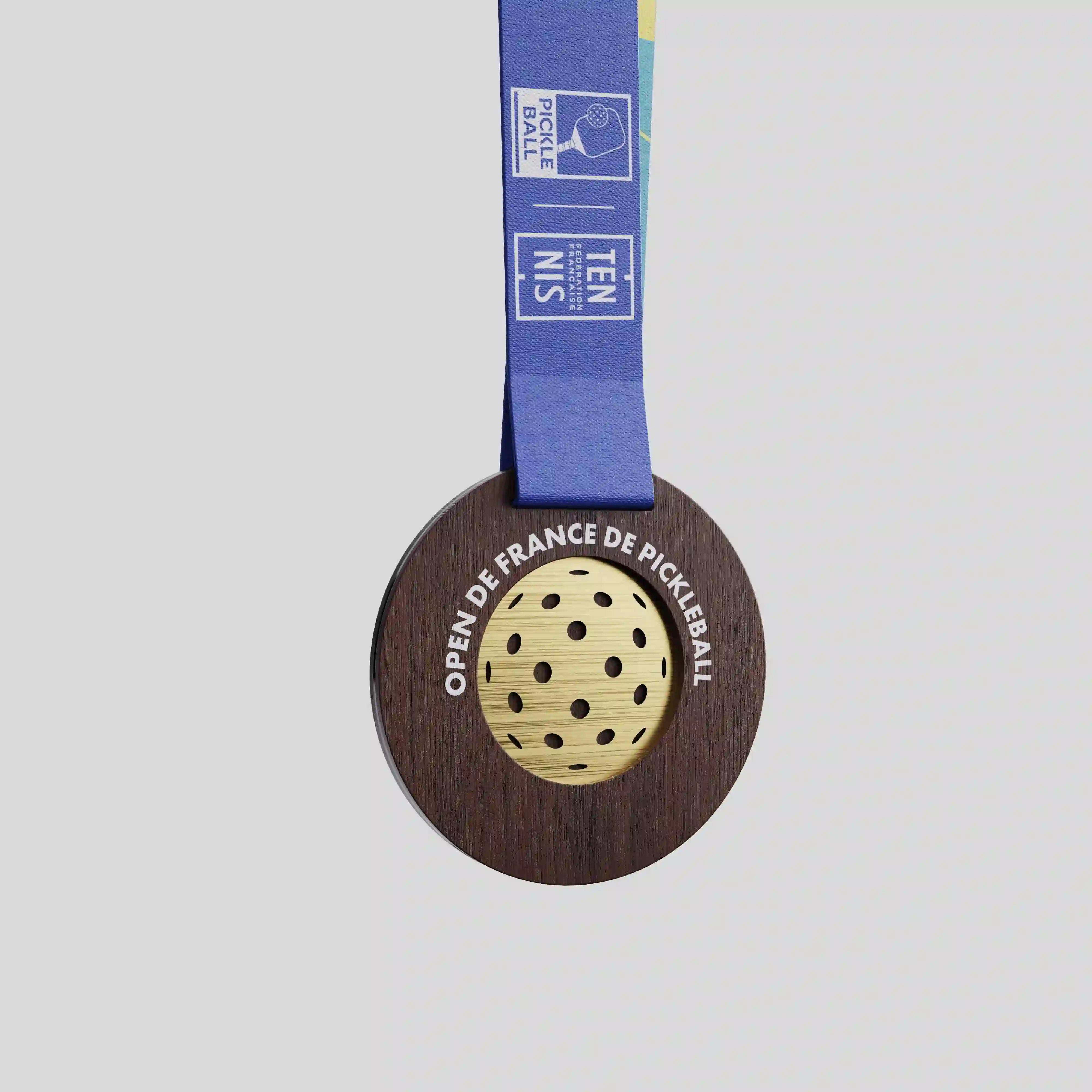 Wood medal for the French Open of Pickleball with gold perforated centre and blue ribbon.